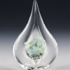 Clear teardrop memorial glass keepsake containing cremation ash, with a suspended inner teardrop and delicate green spiral detail, photographed upright against a dark gradient background.