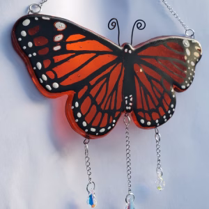 Monarch Butterfly Suncatcher with Cremation Ash, featuring handcrafted orange and black stained glass butterfly wings with white monarch markings and three hanging crystal prisms, photographed against a light background
