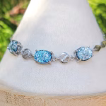 A sterling silver memorial bracelet featuring 3 blue dichroic glass cremation jewels separated by rounds of cubic zirconia.