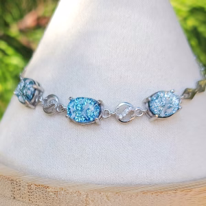 A sterling silver memorial bracelet featuring 3 blue dichroic glass cremation jewels separated by rounds of cubic zirconia.