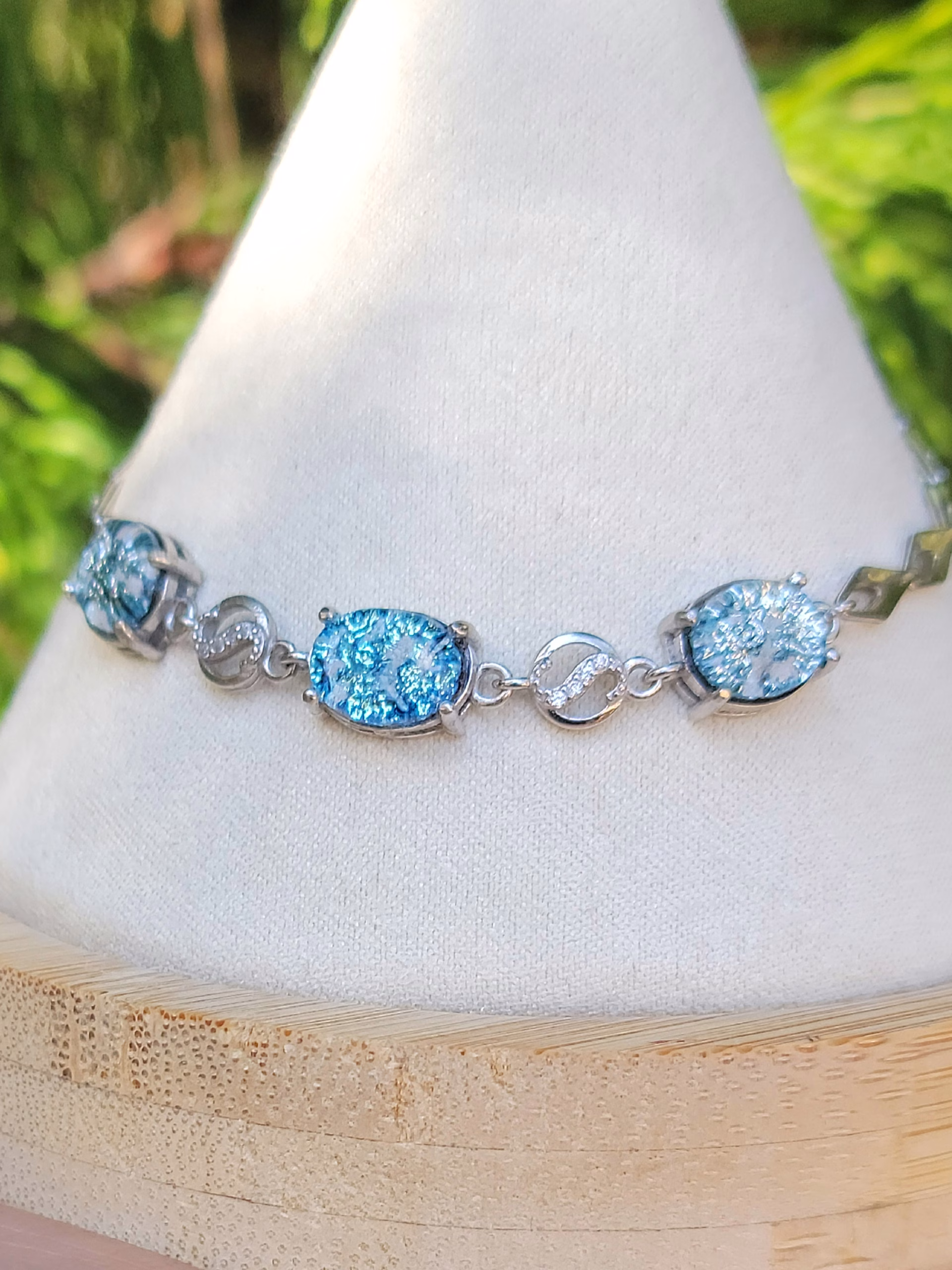 A sterling silver memorial bracelet featuring 3 blue dichroic glass cremation jewels separated by rounds of cubic zirconia.