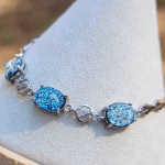 Close-up of a sterling silver triple stone cremation bracelet displayed on a soft white jewelry stand, featuring three round blue memorial glass stones with visible cremation ash, linked by polished silver connectors and a secure clasp.