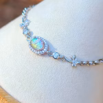 Angled close-up of the Dragonfly Cremation Bracelet featuring a clear rainbow memorial glass oval surrounded by cubic zirconia, set in sterling silver with dragonfly link accents, displayed on a white jewelry stand.