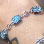 Close-up of a sterling silver triple stone cremation bracelet featuring three oval-shaped blue glass settings with cremation ash, linked by decorative silver connectors, shown worn on the wrist in natural light.