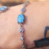 Close-up of the Sands of Time Infinity Cremation Bracelet featuring a blue silver crinkle memorial glass stone set in sterling silver infinity links, worn on the wrist outdoors.