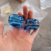 Two handcrafted blue memorial prayer stones made with cremation ash, featuring layered glass patterns and visible ash inclusions, resting side by side in the palm of a hand.