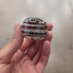 Side view of a handcrafted memorial prayer stone made with cremation ash, showing layered earth-tone glass bands and fine ash inclusions within a smooth, rounded keepsake held in the hand.