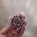 Handcrafted memorial prayer stone made with cremation ash, featuring warm brown layered glass with visible ash inclusions and a smooth, rounded form held gently in the hand.