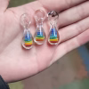 Rainbow Teardrop Cremation Pendants made with cremation ash, featuring layered rainbow colors encased in clear glass, shown as three pendants resting in an open hand