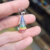 Rainbow Teardrop Cremation Pendant made with cremation ash, featuring layered rainbow colors encased in clear glass, shown held between fingers