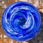 Top view of round blue glass memorial vase with cremation ash and swirling pattern.