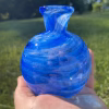 Round blue glass memorial vase with cremation ash held in hand outdoors.
