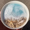 Oceanside Ring Dish with Cremation Ash in a round ceramic dish featuring ocean wave resin design, sandy shoreline, starfish, and seashell memorial details