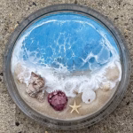 Oceanside Ring Dish with Cremation Ash in a round glass dish featuring ocean wave resin design, sandy shoreline, real seashells, and starfish memorial details