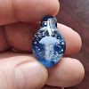 Handcrafted blue glass cremation pendant held between fingers, featuring an intricate white jellyfish suspended in swirling blue glass with shimmering white flecks of encased cremation ashes, shown close-up to highlight detail, depth, and craftsmanship