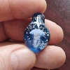 Handcrafted blue glass cremation pendant held between fingers, featuring an intricate white jellyfish suspended inside with shimmering white flecks of encased cremation ashes, shown in a close-up to highlight the pendant’s depth, clarity, and fine craftsmanship