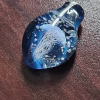 Handcrafted blue glass cremation pendant featuring an intricate white jellyfish suspended inside with swirling white flecks of encased cremation ashes, shown resting on a textured surface in natural light to highlight depth, clarity, and color