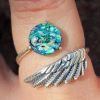 Angel wing cremation ring with round Aqua Crinkle glass stone containing cremation ashes, shown worn on finger with detailed silver wing band.