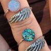Two Angel Wing Cremation Rings worn on fingers, featuring sterling silver wing bands and round memorial glass stones in blue, teal, and iridescent tones with cremation ash fused into the glass