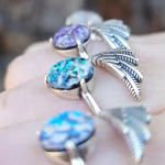 Side view of Angel Wing Cremation Rings showing sterling silver wing bands and round memorial glass stones in blue, teal, and purple with cremation ash fused into each stone