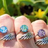 Three Angel Wing Cremation Rings worn across fingers, featuring sterling silver wing bands and round memorial glass stones in blue, teal, and purple with cremation ash fused into each glass stone