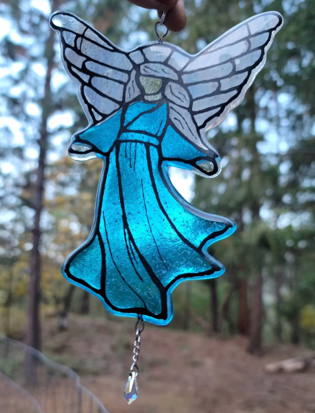Guardian Angel suncatcher made with cremation ash, featuring translucent blue stained glass robes, silver-toned angel wings, and a hanging crystal accent, photographed outdoors in natural light.
