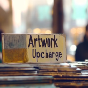 Artwork upcharge sign displayed on a tabletop, indicating an additional fee for custom artwork or design work.