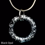 Halo Cremation Pendant in black opal, featuring a dark glass ring with white and gray ash inclusions, suspended from a silver chain against a black background.
