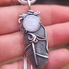 Close-up of the Boho Feather Cremation Pendant in sterling silver, featuring a feather memorial pendant with a white cremation ash glass cabochon held in the palm of a hand