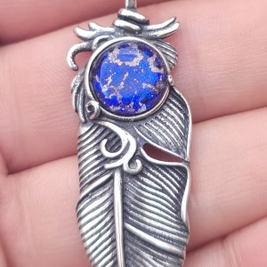 Close-up of the Boho Feather Cremation Pendant in sterling silver, featuring a feather memorial pendant with a blue cremation ash glass cabochon displayed against a hand for scale