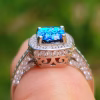 Side-angle close-up of the Cremation Ring with Square Halo Band on a finger, highlighting the blue silver crinkle glass center stone, square halo of cubic zirconia accent stones, decorative gallery details, and a sterling silver band with cubic zirconia accents.