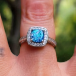 Cremation Ring with Square Halo Band worn on a finger, featuring a blue silver crinkle glass center set in a square halo of cubic zirconia stones on a silver band.