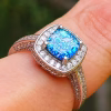 Cremation Ring with Square Halo Band worn on a finger, featuring a blue silver crinkle glass center set in a square halo of cubic zirconia stones on a silver band.