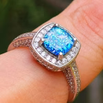 Cremation Ring with Square Halo Band worn on a finger, featuring a blue silver crinkle glass center set in a square halo of cubic zirconia stones on a silver band.