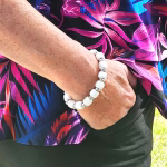 Eternity Cremation Bracelet with cremation ash, featuring white bead design with silver spacer accents, worn on wrist against a colorful floral blouse background