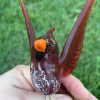 Angled front view of a handcrafted glass cardinal memorial sculpture with cremation ash visible inside the red glass body, held in hand over green grass.