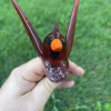Top-down view of a handcrafted glass cardinal memorial sculpture with cremation ash visible inside the red glass body, held in hand over green grass.