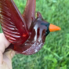 Handcrafted glass cardinal memorial sculpture with cremation ash suspended in the red glass body, wings extended, held in hand outdoors.