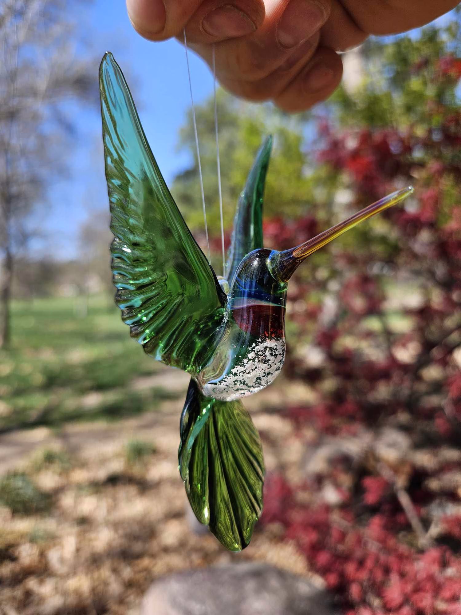 Handmade green glass hummingbird with raised wings and cremation ash visible in the body.