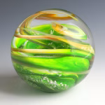 Ocean Memorial Cremation Paperweight featuring a hand-blown glass sphere with vibrant green layers, flowing gold ribbons, and subtle white accents encased in clear glass.