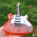 Memorial Guitar with Cremation Ash shown from a low, tilted front angle with translucent red glass body, white pickguard, black glass neck, and hand holding the guitar outdoors