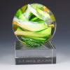 Ocean Memorial Cremation Paperweight featuring a round hand-blown glass sphere with flowing green, white, and yellow swirls, displayed on a clear engraved glass base with a name and memorial dates.