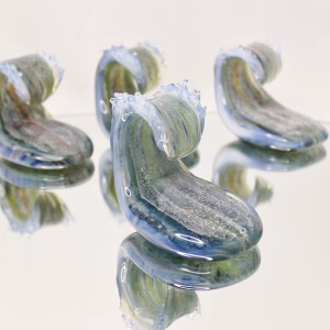 Crashing Wave Memorial Keepsake with cremation ash in blue, seafoam green, and clear glass, shown as a group of sculpted waves on a mirrored surface in a studio setting