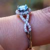 Close-up side view of an Infinity Cremation Ring on a finger, featuring a blue memorial stone set in a prong halo with sparkling cubic zirconia. The band forms an elegant infinity loop lined with stones, with a blurred natural background highlighting the ring’s detail.