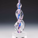 Hand-blown glass Legacy Flame cremation sculpture featuring swirling pink and blue ribbons encased in clear glass, set on a polished square glass base, created as a vibrant and meaningful memorial keepsake.