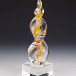 Pink and gold Legacy Flame cremation ash sculpture with intertwined shimmering ribbons encased in clear hand-blown glass, mounted on a square glass base as a modern memorial keepsake.