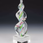 Aqua, pink, and green Legacy Flame cremation ash sculpture featuring a hand-blown glass design with swirling multicolor ribbons suspended in clear glass, set on a polished square glass base as a modern memorial keepsake.