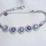 Studio image of the Dichroic Halo Cremation Bracelet featuring five round blue and purple dichroic memorial glass stones, each surrounded by a halo of clear cubic zirconia, set in sterling silver with an adjustable clasp on a white background.