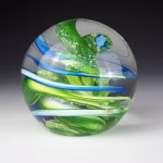 Ocean Memorial Cremation Paperweight featuring a hand-blown glass sphere with layered green tones, soft white accents, and flowing blue ribbons suspended within clear glass.