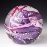 Ocean Memorial Cremation Paperweight featuring a hand-blown glass sphere with layered lavender and deep purple glass, accented by soft pink ribbons and delicate white inclusions suspended in clear glass.